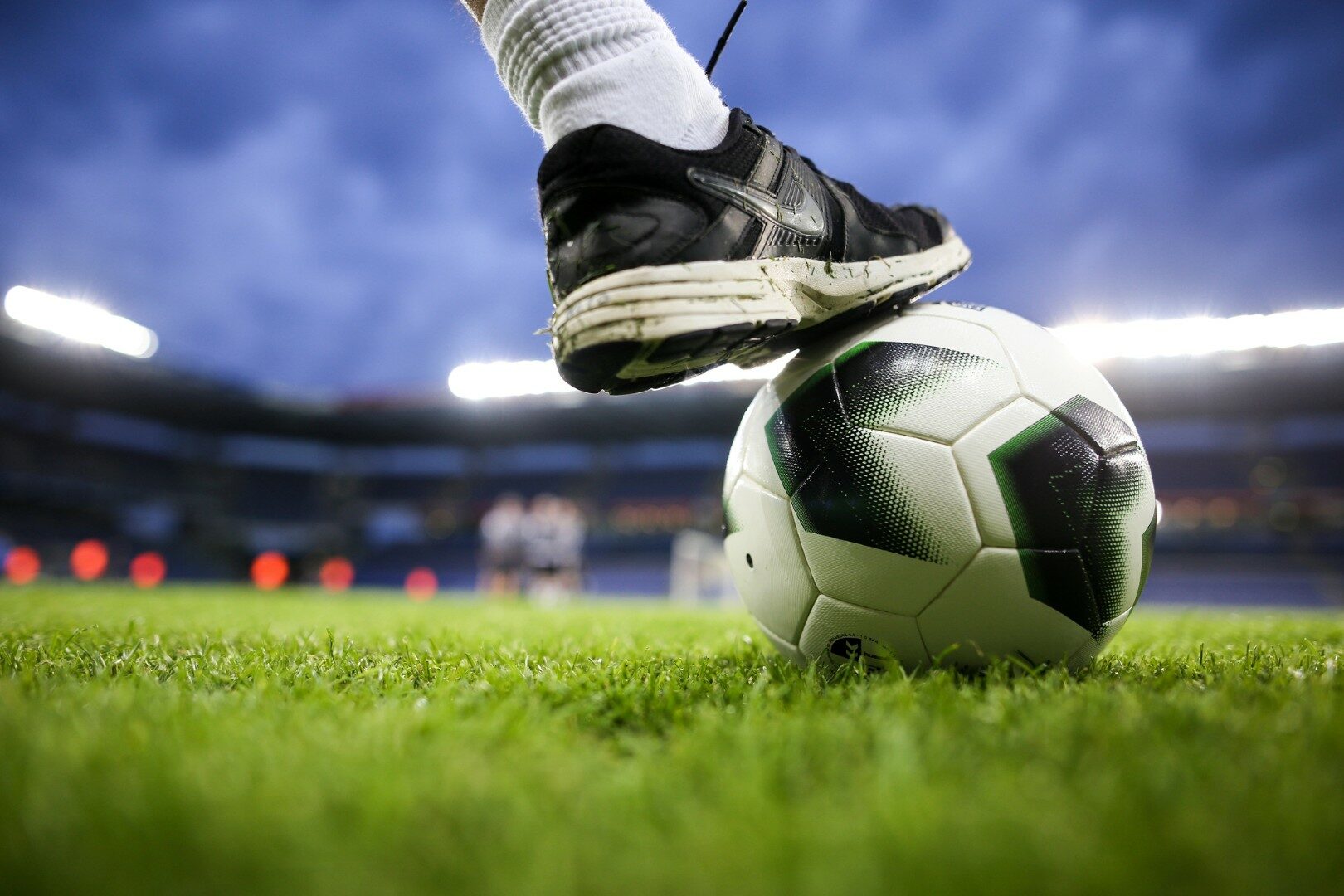 Een historisch beeld van het oude HFC Haarlem-stadion met supporters op de tribune, rood-blauwe vlaggen en avondlicht over het veld.