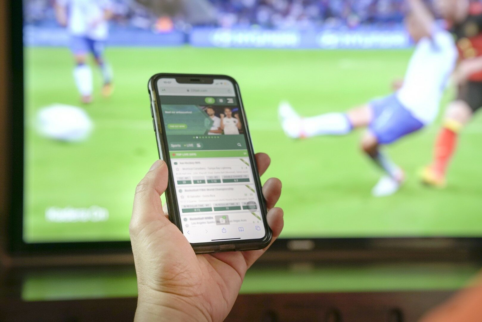 Voetbalwedstrijd op tv bekijken en weddenschappen sluiten op de app van bookmakers via een mobiele telefoon. close-up schot.
